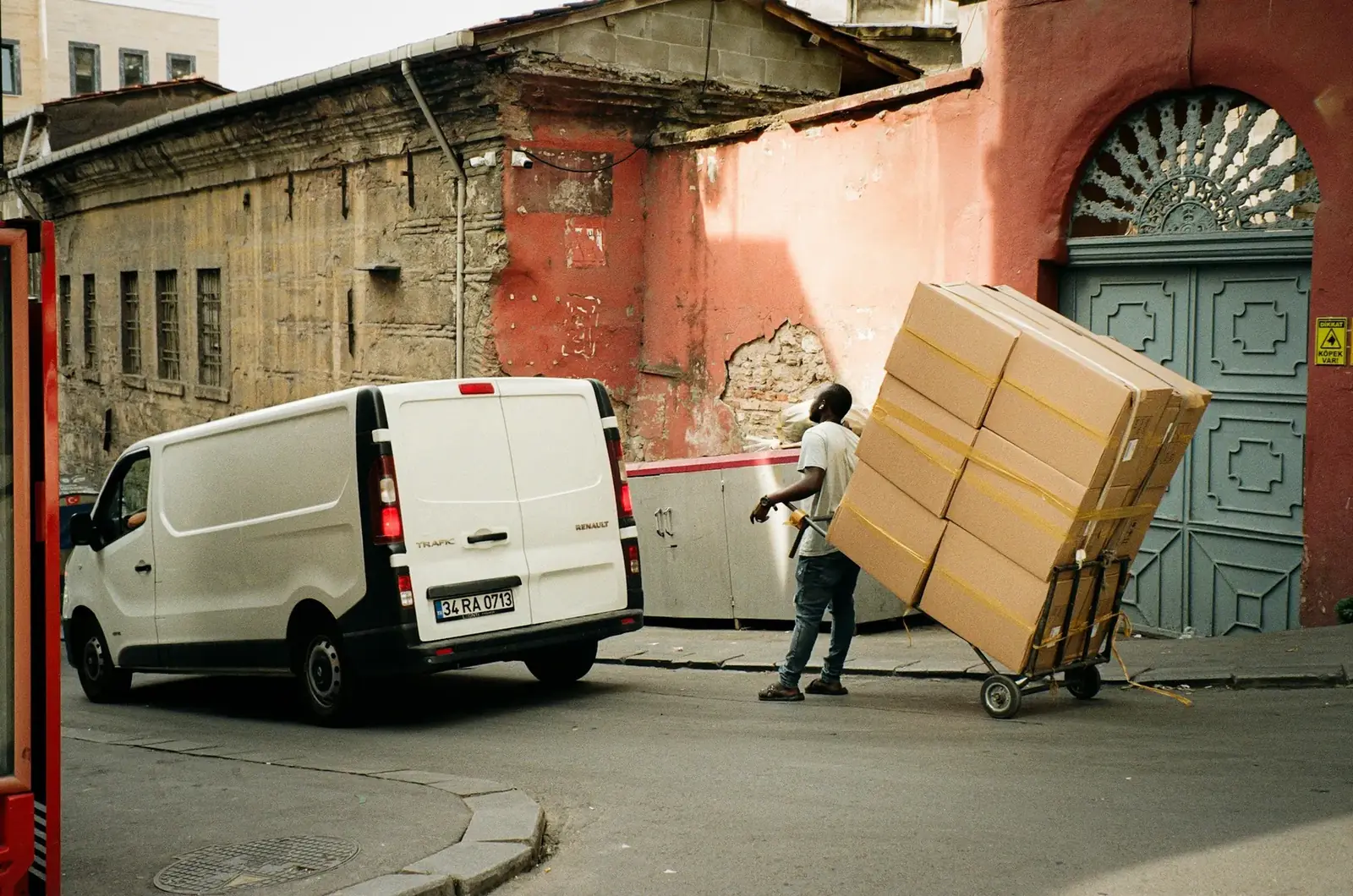 Mover wheeling a tall stack of boxes on a hand truck beside a white van